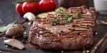 Juicy grilled steak with herbs and seasoning on a rustic wooden board.