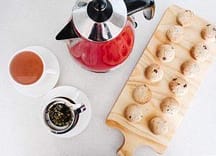 Delicious macarons and a cup of tea with a French press coffee on a white surface.
